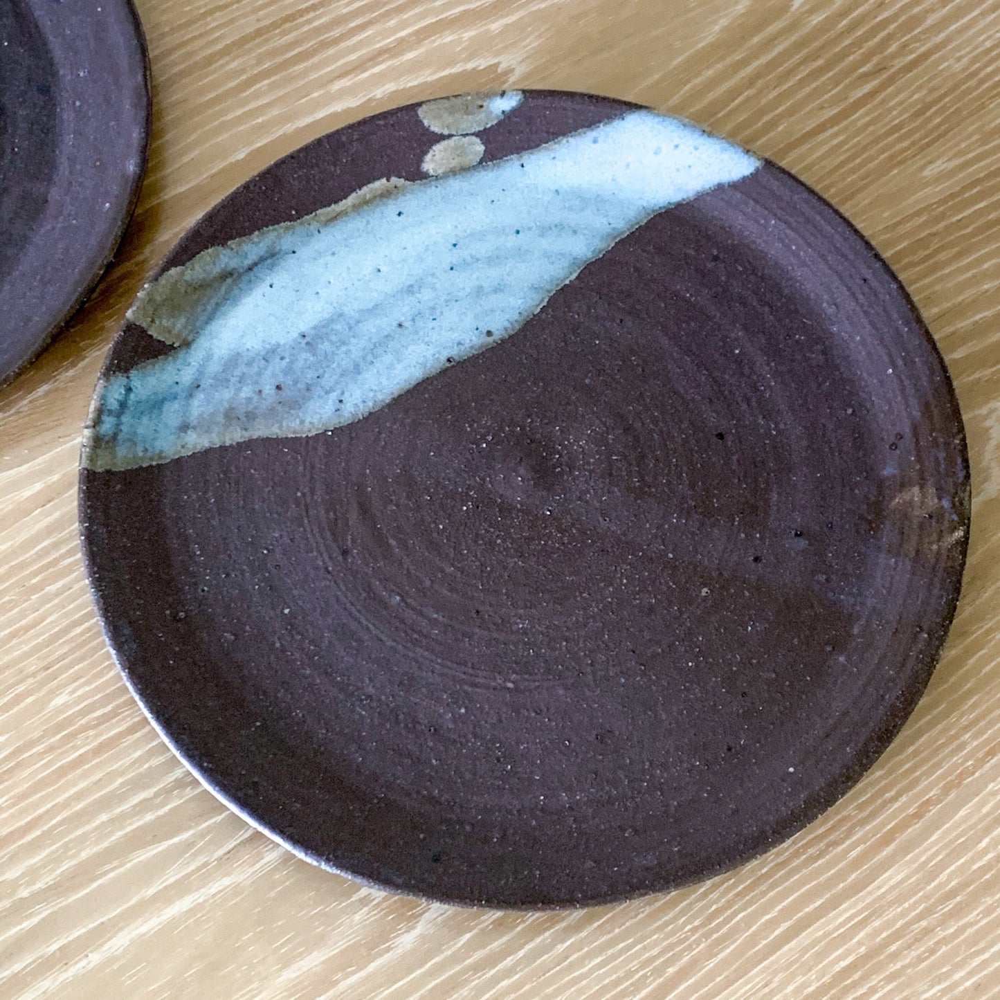 Pottery plate in matt brown color with shiny blue splash