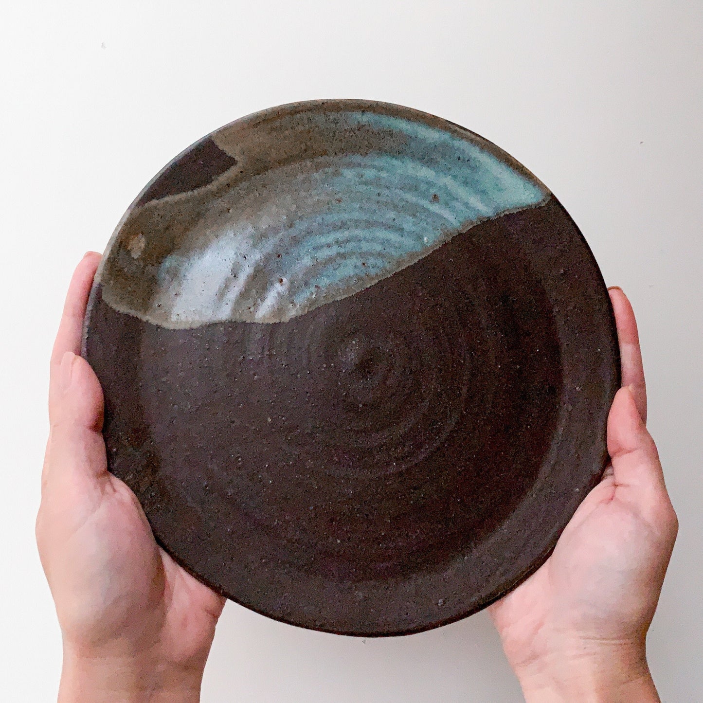 Pottery plate in matt brown color with shiny blue splash